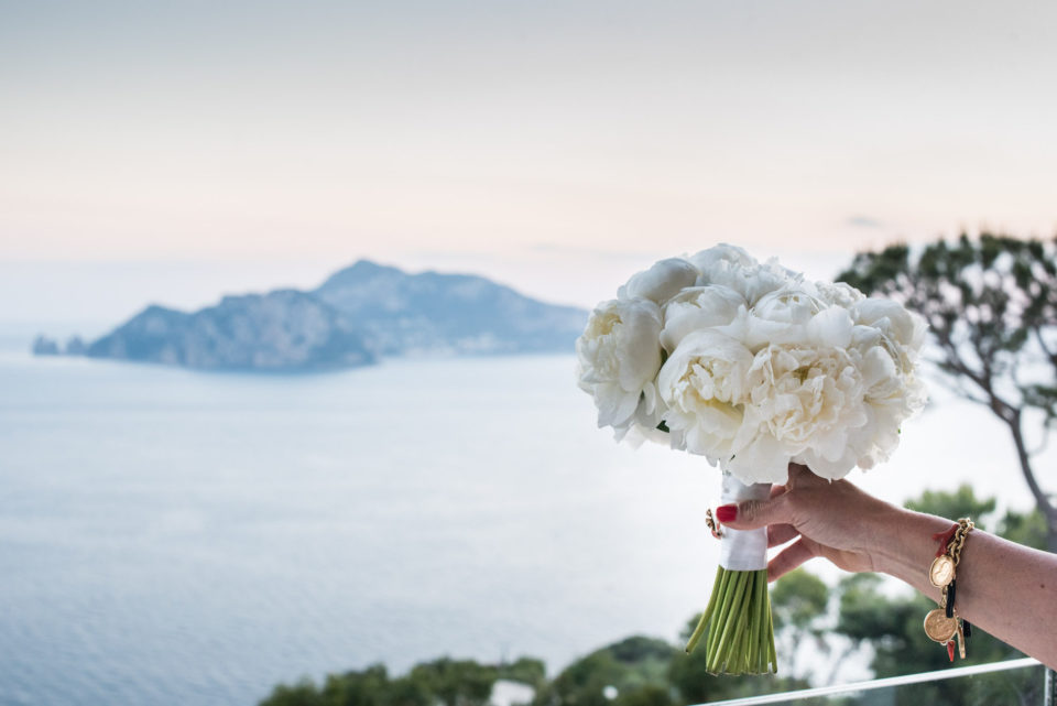 capri island in the background with a bridal bouquet made with white peonies