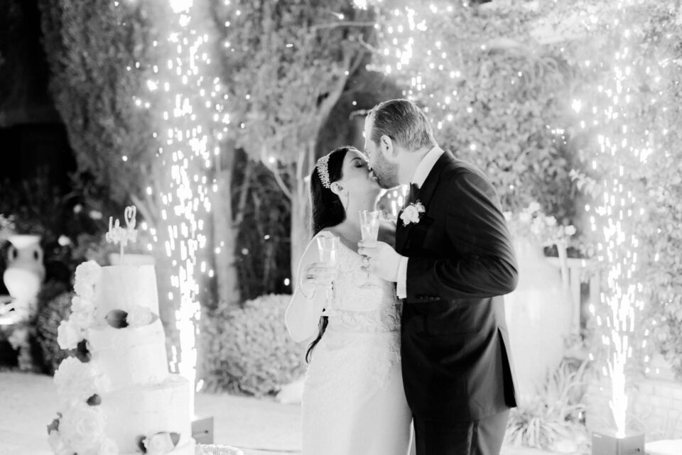Bride and groom kissing in front of their wedding cake with the sparkles behind them