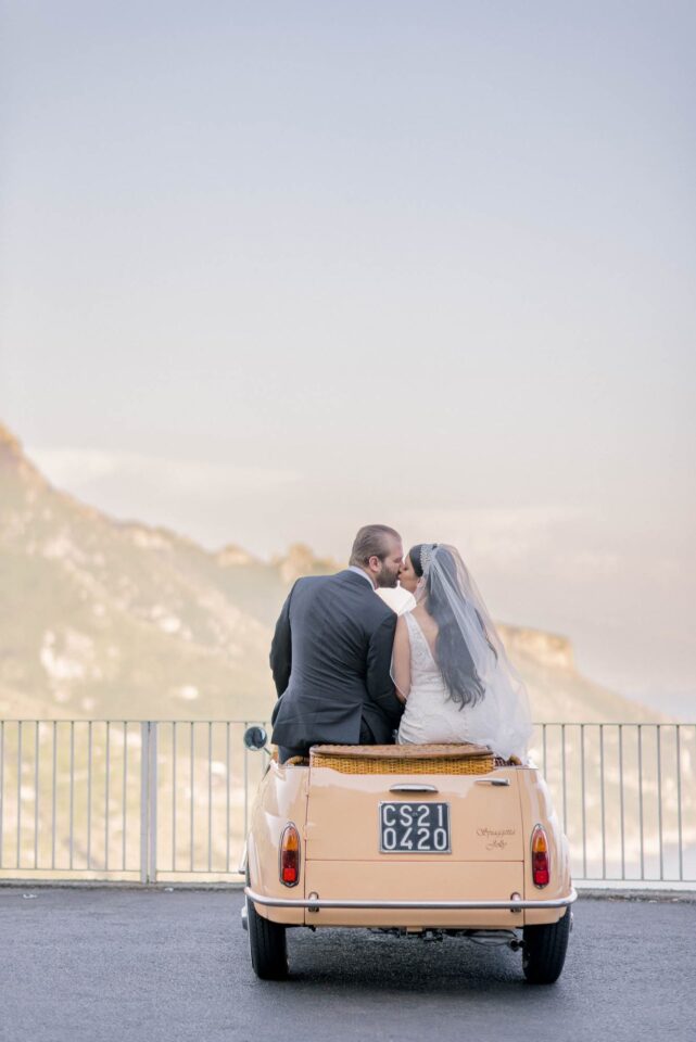 bride and groom kissing while seated on a fiat 500